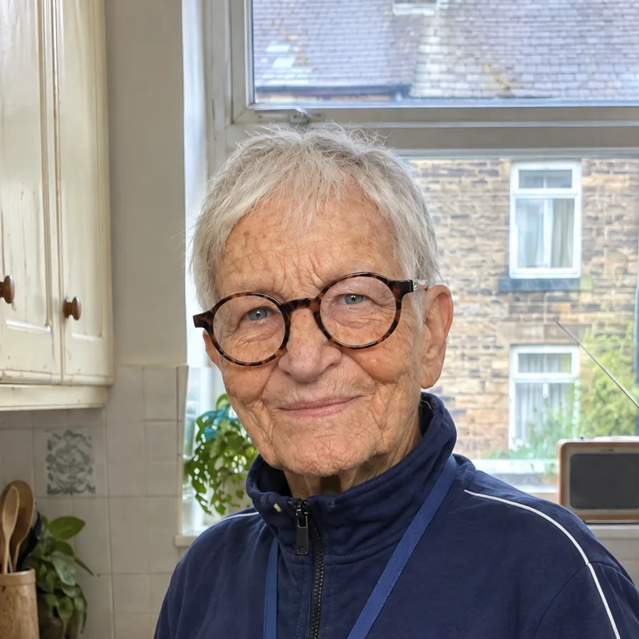 Edith Hartley, wearing round tortoiseshell glasses and a navy tracksuit top, standing in her kitchen.